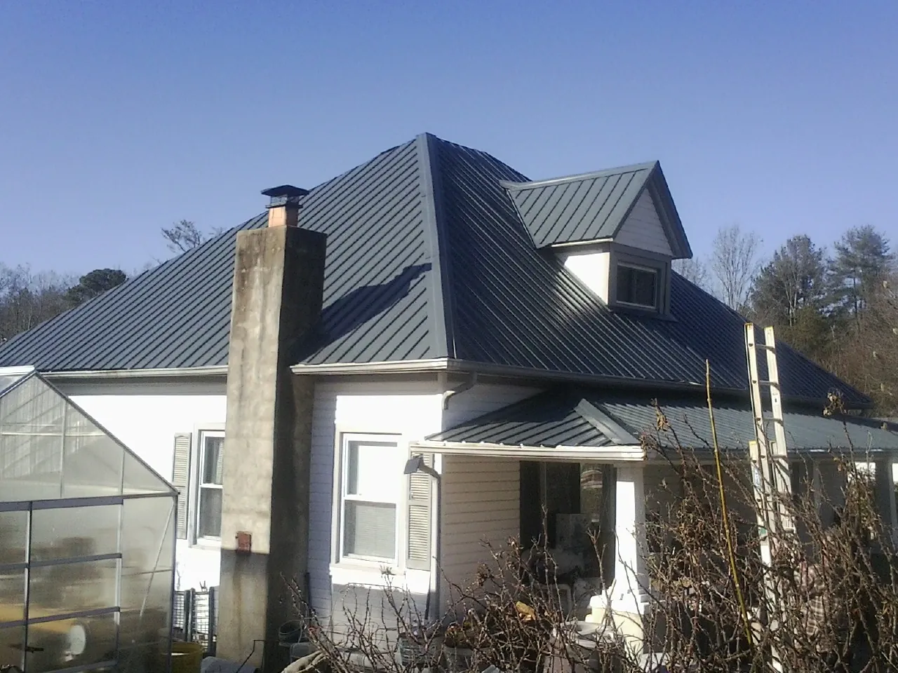 Dark blue standing seam metal roof on a white farmhouse with dormer — Slate & Tile Roof Repair by Roofing Brothers in Chilton