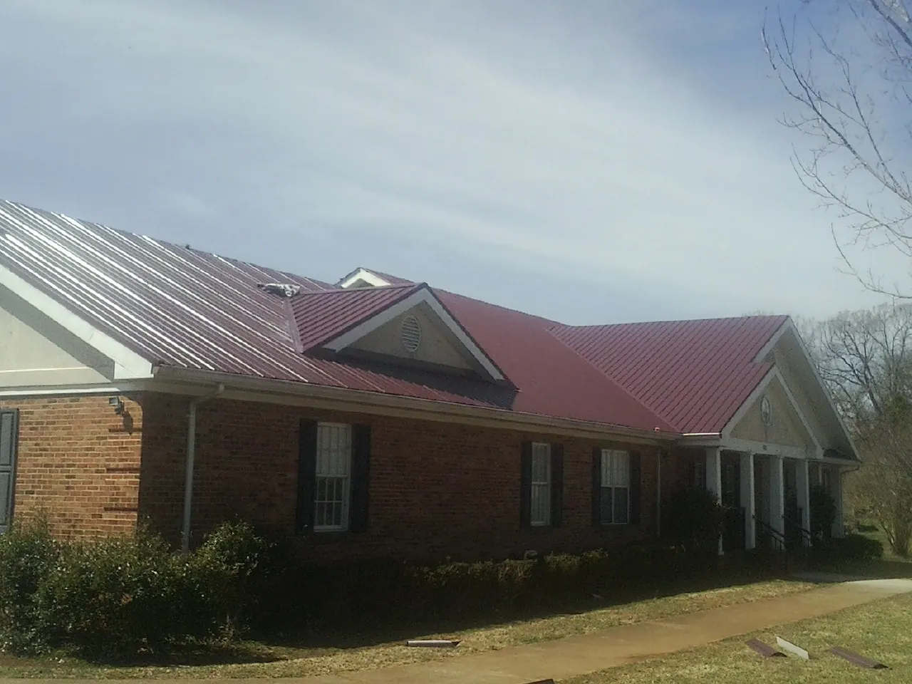 Red metal roof with gabled entries on a long brick building, from a Hail Damage Roof Repair job in Chilton