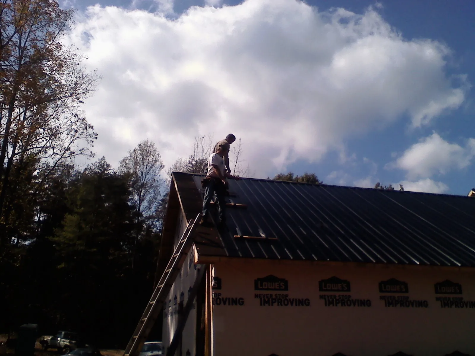 Roofer fastening dark metal panels high against a cloudy sky, from a Roof Inspection job in Chilton
