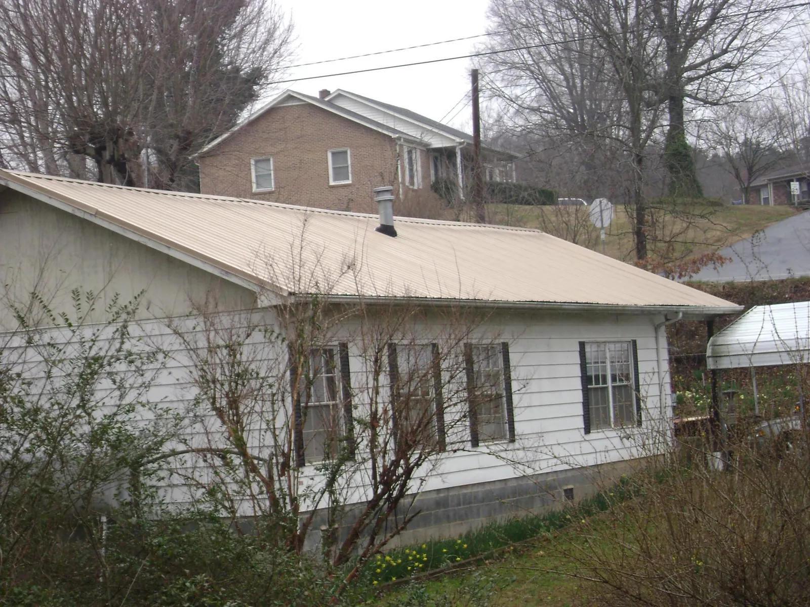 Tan metal roof on a white sided house set into a hillside — Commercial Roofing by Roofing Brothers in Chilton