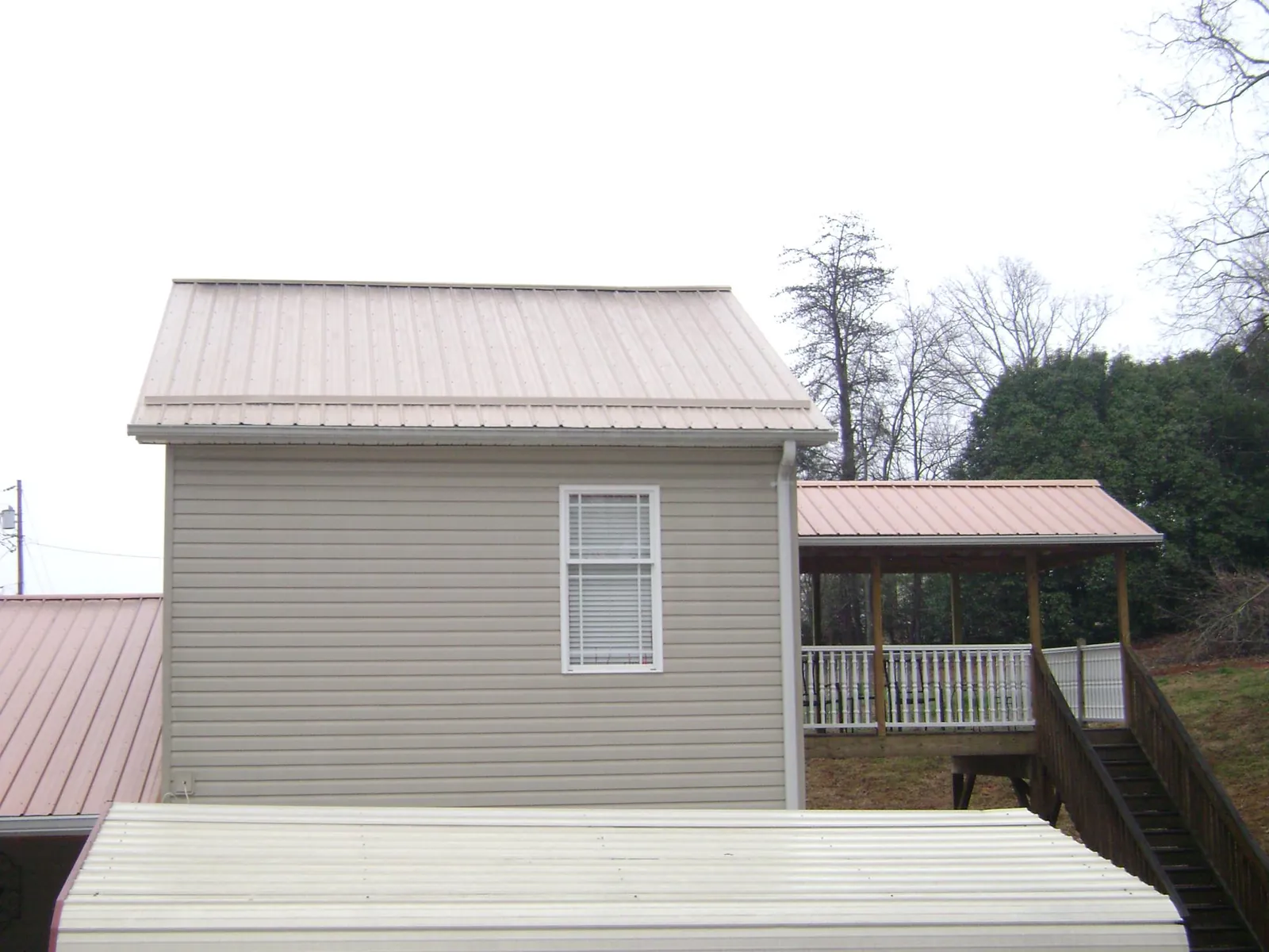 Tan metal roofs on a two story addition and attached porch, from a Roof Replacement job in Chilton